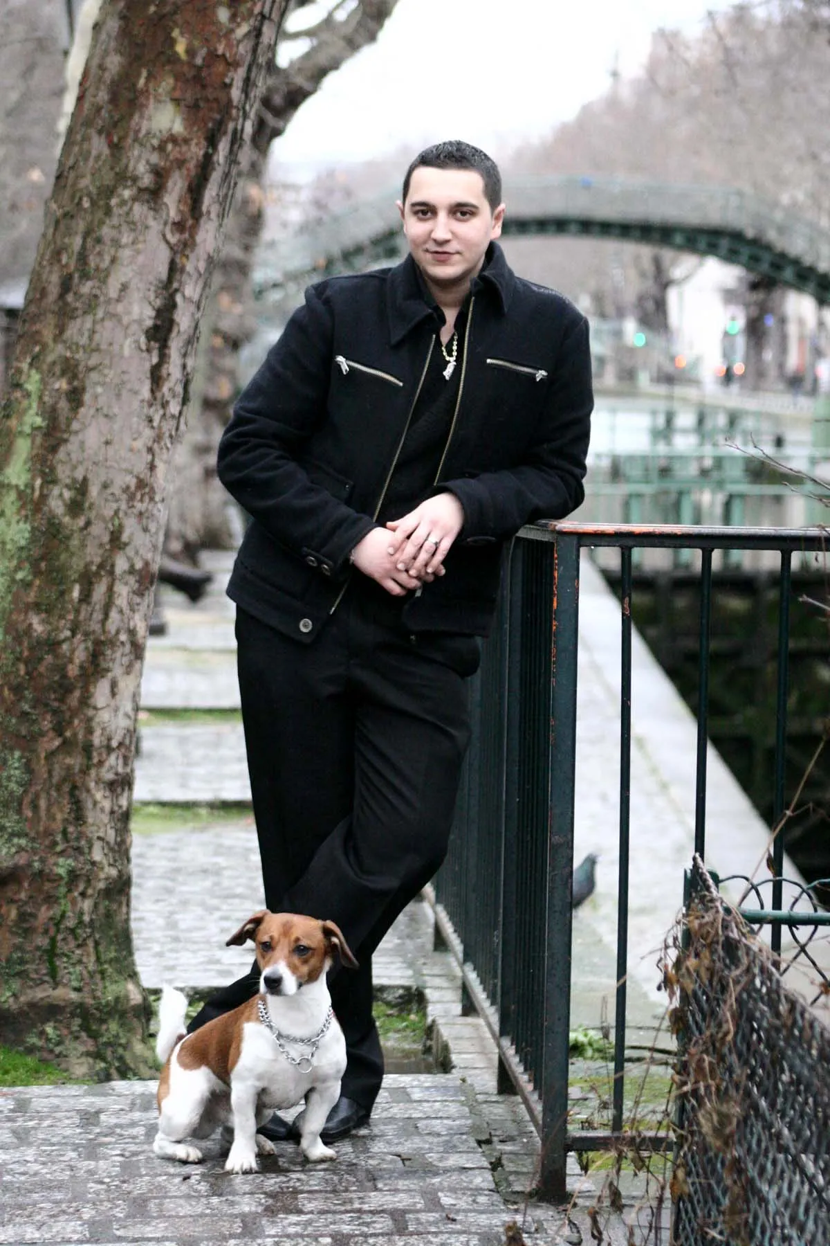 A man standing by a canal railing with his Jack Russell terrier at his feet