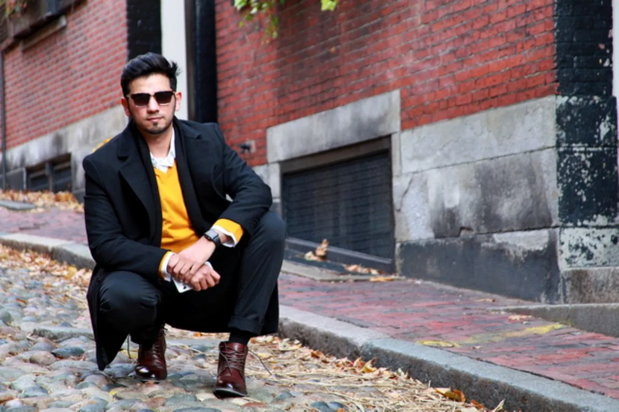 Portrait of a man crouching on a cobblestone street lined with brick buildings