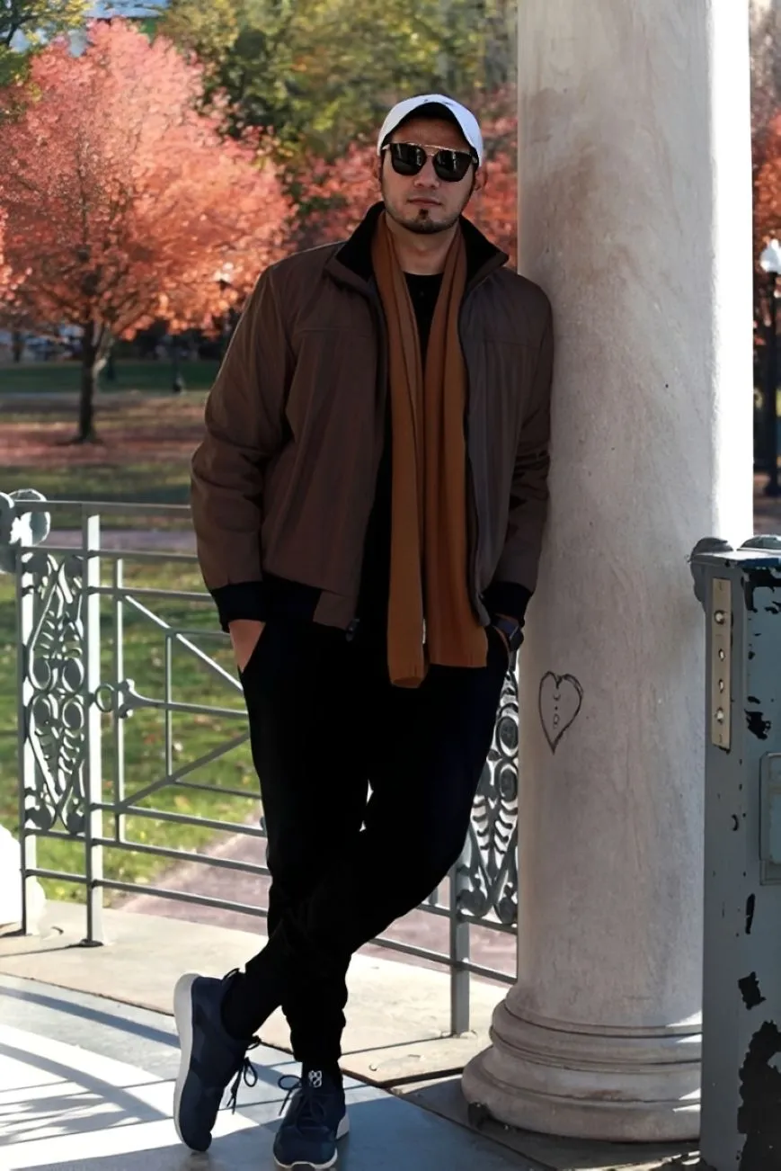 Outdoor portrait of a man beside a bandstand column with autumn trees behind him